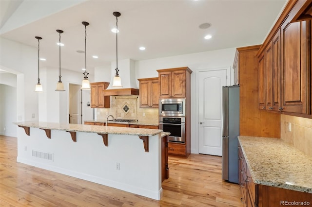 kitchen featuring stainless steel appliances, a kitchen bar, brown cabinets, tasteful backsplash, and recessed lighting