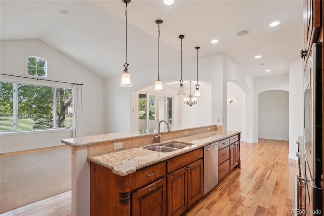 kitchen featuring stainless steel dishwasher, a sink, arched walkways, brown cabinetry, and light stone countertops