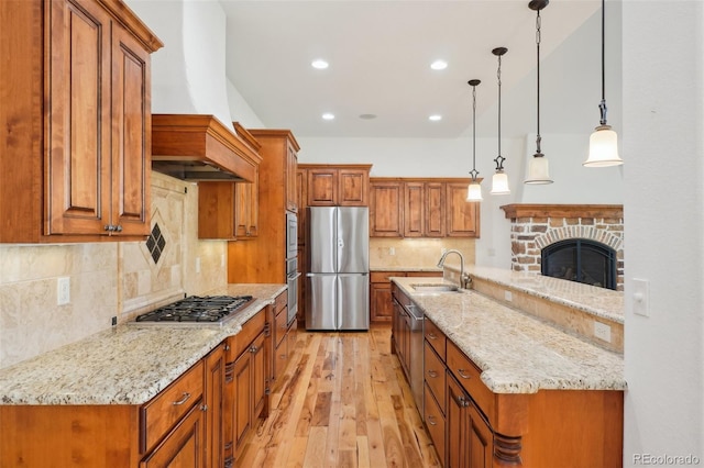 kitchen with appliances with stainless steel finishes, brown cabinets, custom exhaust hood, a sink, and light wood-style flooring
