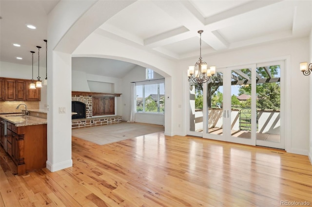unfurnished dining area featuring light wood finished floors, a fireplace, a chandelier, a sink, and beam ceiling