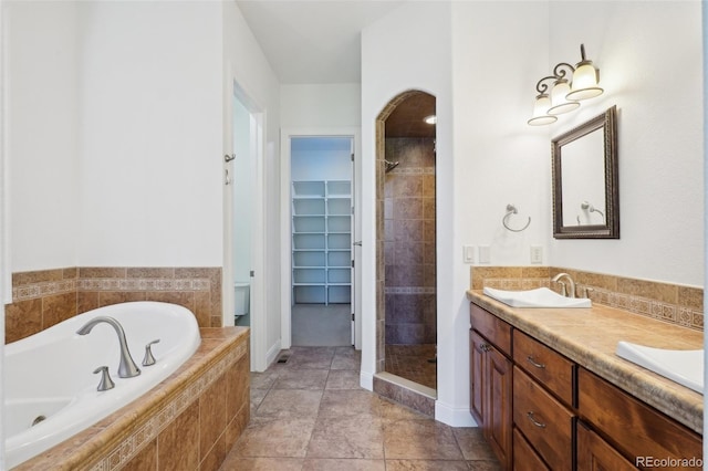 bathroom with a walk in closet, a garden tub, a shower stall, double vanity, and baseboards
