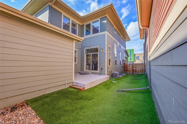 rear view of house with central air condition unit, a patio area, fence, and a lawn