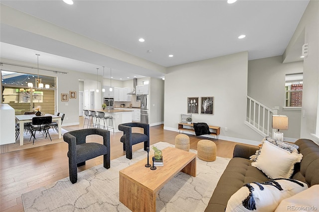 living area featuring a chandelier, recessed lighting, baseboards, stairs, and light wood-style floors