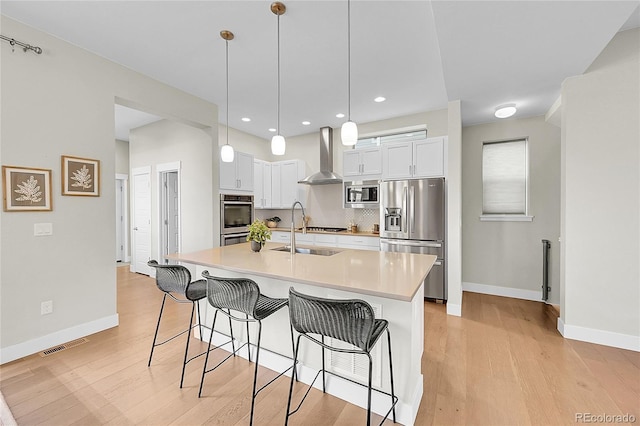 kitchen with a breakfast bar area, appliances with stainless steel finishes, wall chimney exhaust hood, light wood finished floors, and tasteful backsplash