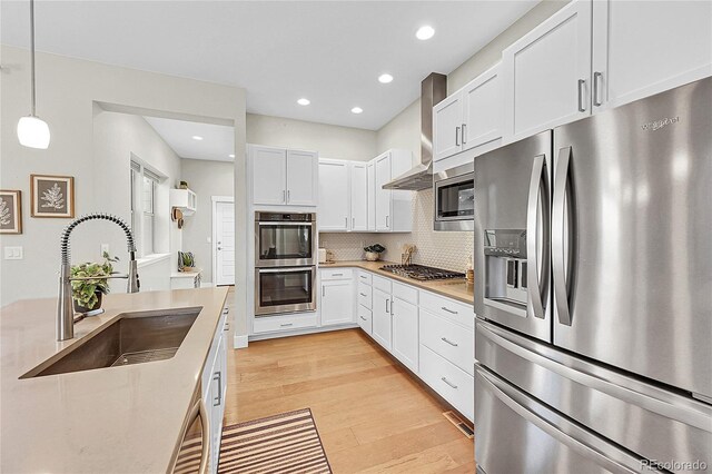 kitchen featuring light wood finished floors, backsplash, appliances with stainless steel finishes, white cabinetry, and a sink