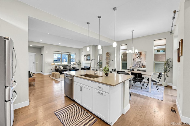 kitchen with light wood-style flooring, appliances with stainless steel finishes, a kitchen island with sink, white cabinets, and a sink