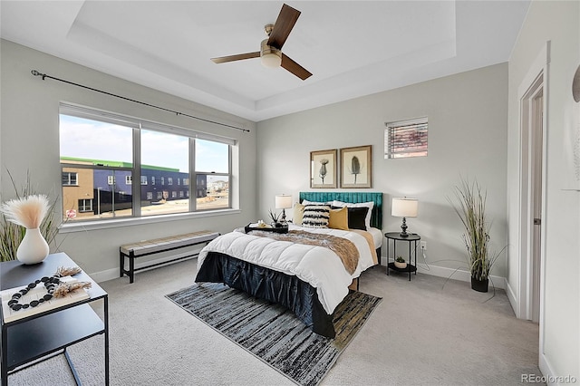 carpeted bedroom with a ceiling fan, a tray ceiling, and baseboards