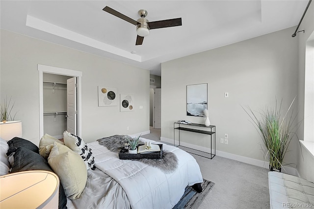 bedroom featuring light carpet, baseboards, ceiling fan, a spacious closet, and a tray ceiling