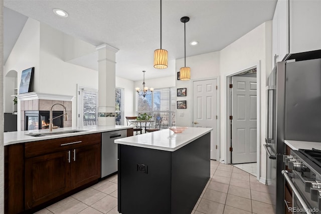 kitchen featuring high end appliances, sink, light tile patterned floors, hanging light fixtures, and an island with sink