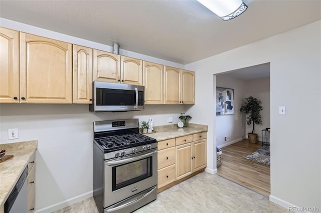 kitchen with light brown cabinets, appliances with stainless steel finishes, light countertops, and baseboards