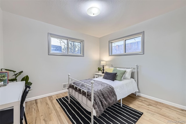 bedroom featuring visible vents, baseboards, a textured ceiling, and light wood-style flooring