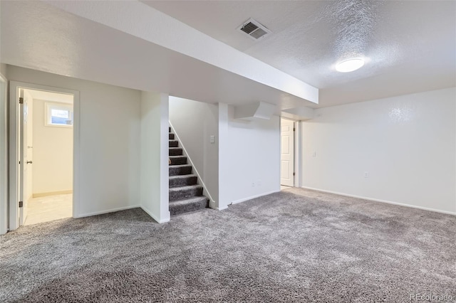 finished basement with visible vents, carpet flooring, a textured ceiling, and stairs