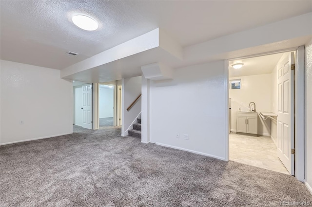 finished basement featuring visible vents, stairs, light carpet, a textured ceiling, and a sink