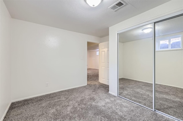 unfurnished bedroom featuring visible vents, a textured ceiling, a closet, carpet floors, and baseboards