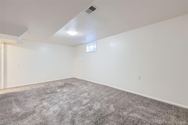 below grade area featuring visible vents, a textured ceiling, baseboards, and carpet