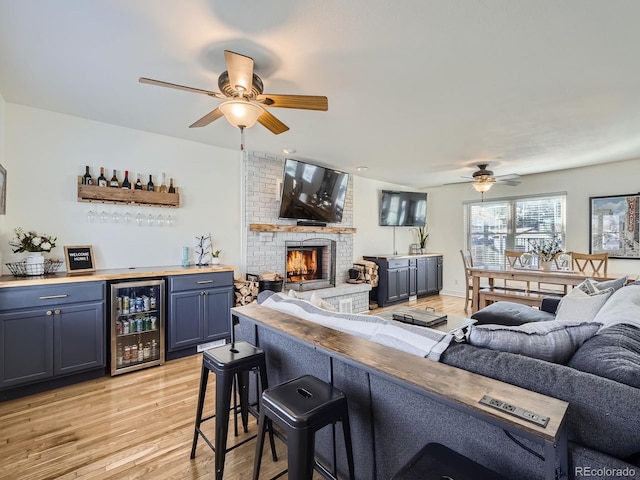 living room with wine cooler, bar area, light wood-type flooring, ceiling fan, and a fireplace