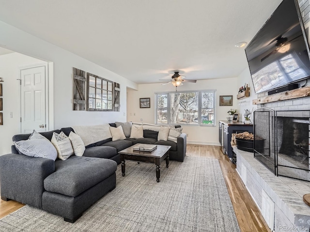 living room with ceiling fan, a brick fireplace, and light hardwood / wood-style flooring