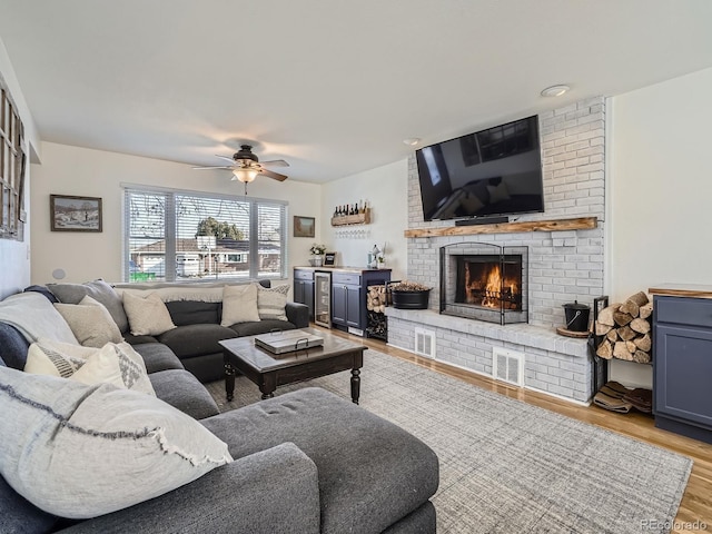 living room featuring a fireplace, light hardwood / wood-style floors, beverage cooler, and ceiling fan