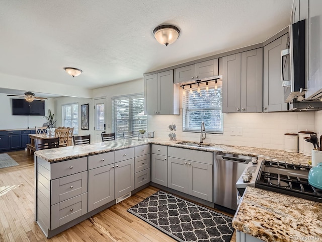 kitchen with stainless steel appliances, light stone countertops, sink, and kitchen peninsula