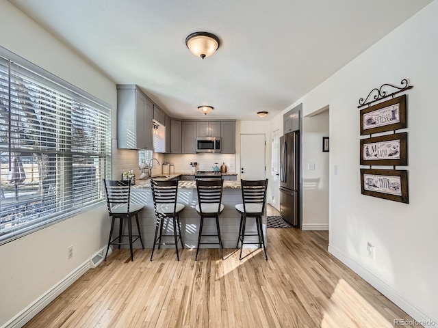 kitchen featuring sink, gray cabinetry, stainless steel appliances, a kitchen breakfast bar, and light hardwood / wood-style floors