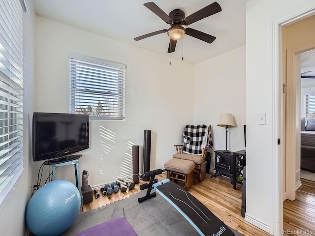 exercise room featuring a wood stove, ceiling fan, and light hardwood / wood-style flooring