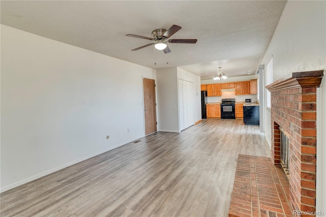 unfurnished living room with a brick fireplace, baseboards, light wood-type flooring, ceiling fan with notable chandelier, and a textured ceiling