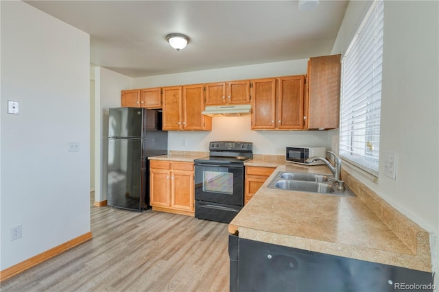 kitchen with under cabinet range hood, light countertops, light wood-style floors, black appliances, and a sink