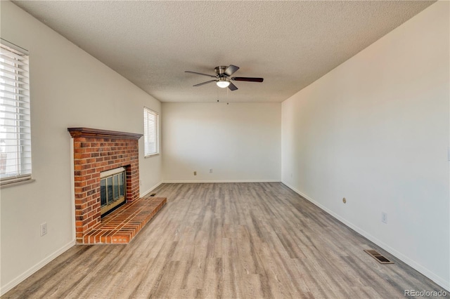 unfurnished living room with a brick fireplace, a textured ceiling, ceiling fan, and wood finished floors