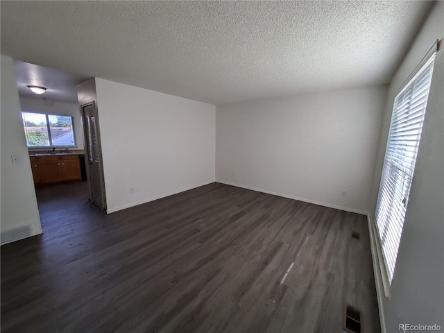 unfurnished room featuring baseboards, dark wood-style floors, visible vents, and a textured ceiling