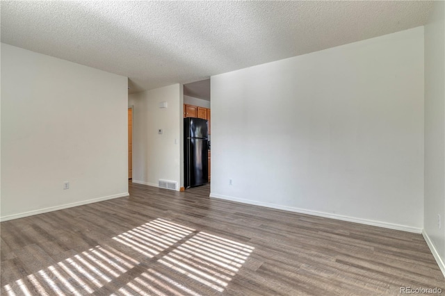 empty room with a textured ceiling, wood finished floors, visible vents, and baseboards