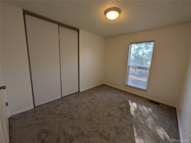 unfurnished bedroom featuring visible vents, baseboards, carpet, a closet, and a textured ceiling