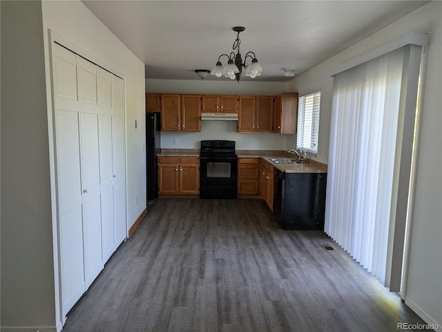 kitchen with wood finished floors, a sink, black appliances, under cabinet range hood, and decorative light fixtures