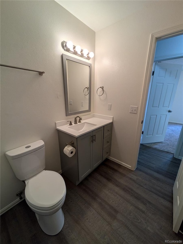 half bathroom with vanity, toilet, wood finished floors, and baseboards