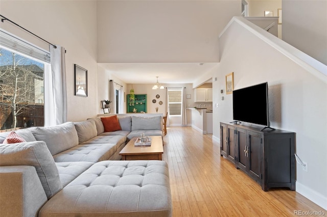 living area with a high ceiling, plenty of natural light, baseboards, and light wood-type flooring