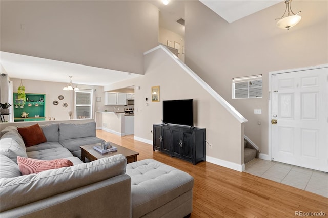 living room featuring baseboards, light wood-style floors, an inviting chandelier, and stairs