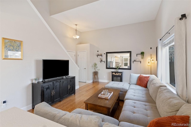 living area featuring stairway, baseboards, light wood-style floors, and a towering ceiling