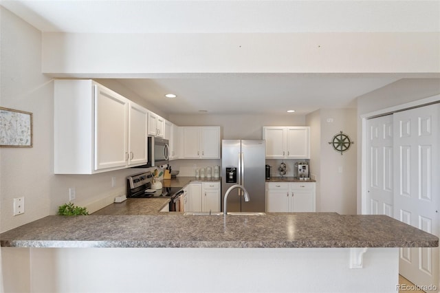 kitchen featuring a peninsula, recessed lighting, a sink, appliances with stainless steel finishes, and white cabinetry