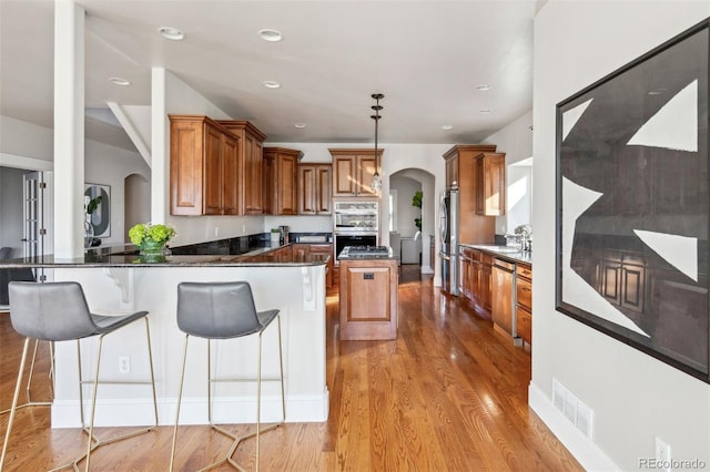 kitchen featuring a kitchen bar, sink, kitchen peninsula, pendant lighting, and light hardwood / wood-style floors