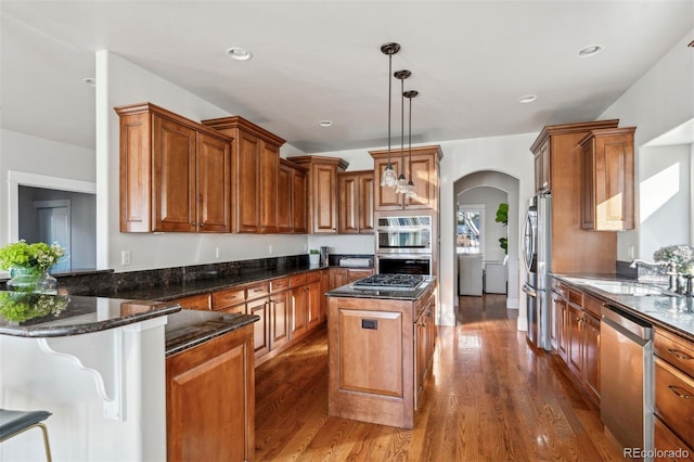 kitchen with sink, appliances with stainless steel finishes, dark stone countertops, hanging light fixtures, and a center island