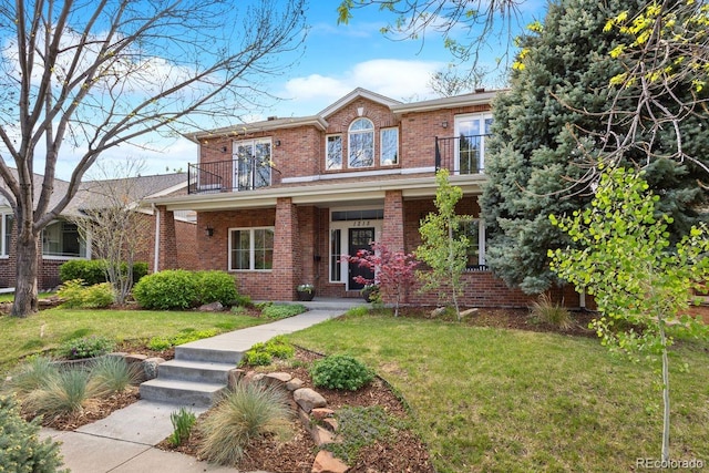 view of front of home with a balcony, brick siding, and a front lawn