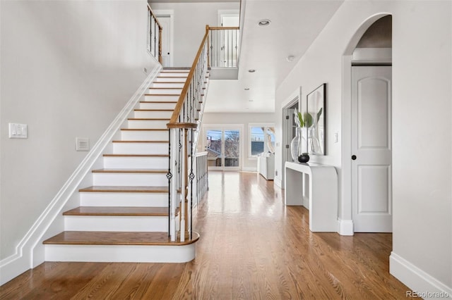 stairs featuring arched walkways, wood finished floors, and baseboards