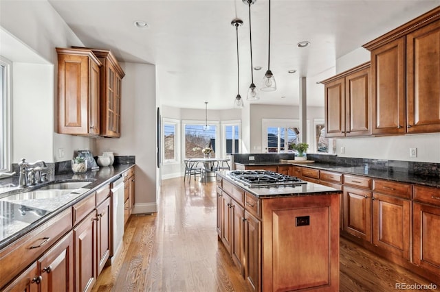 kitchen featuring appliances with stainless steel finishes, a sink, wood finished floors, brown cabinetry, and pendant lighting