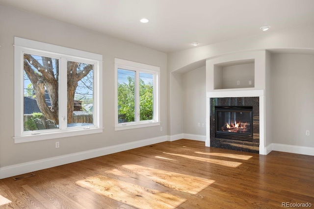 unfurnished living room with baseboards, wood finished floors, a tiled fireplace, and recessed lighting