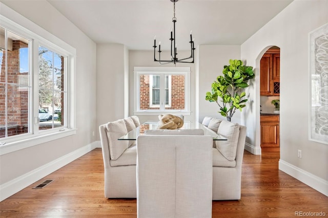 dining area featuring a chandelier, arched walkways, baseboards, and light wood-style floors