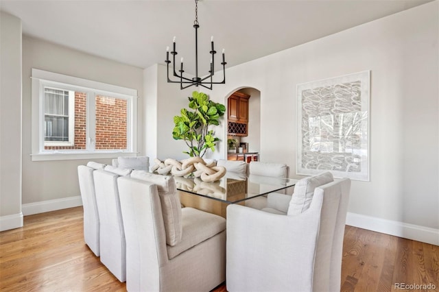 dining room featuring a chandelier, baseboards, light wood-style floors, and arched walkways