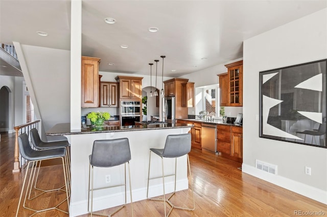 1215 S Ogden St, Denver, CO 80210 - kitchen featuring stainless steel appliances, brown cabinets, a kitchen breakfast bar, light wood-style floors, and a peninsula