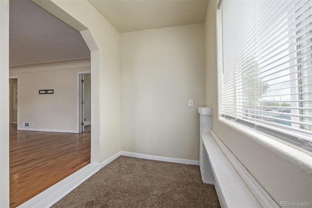 corridor with baseboards, arched walkways, carpet floors, and visible vents