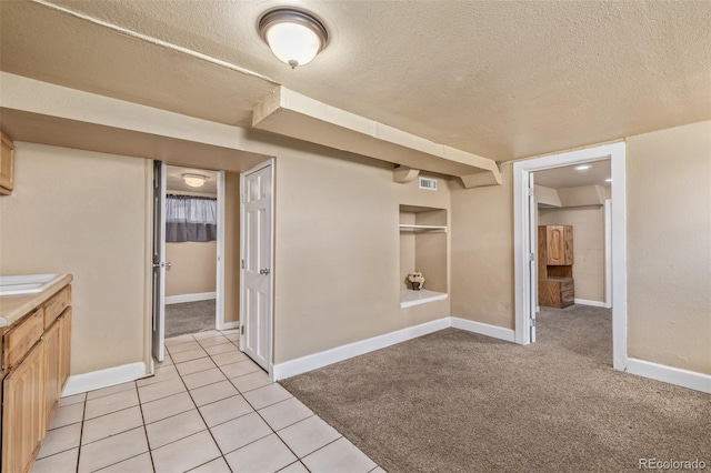 interior space featuring light colored carpet, a textured ceiling, visible vents, and baseboards