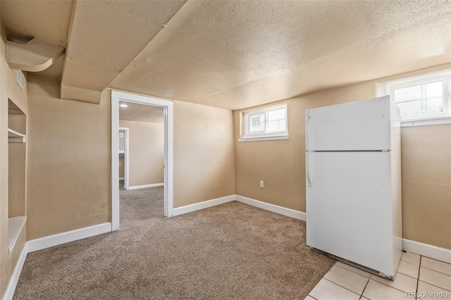 basement featuring freestanding refrigerator, a textured ceiling, and a wealth of natural light