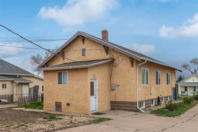 rear view of house with fence, stucco siding, and a chimney